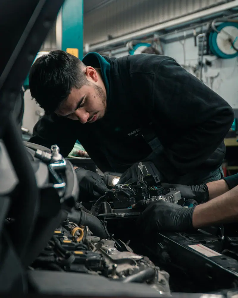 Mechaniker beugt sich über den geöffneten Motorraum und arbeitet mit Handschuhen am Motor